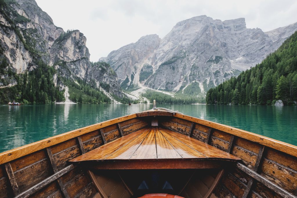 A wooden boat on an emerald lake surrounded by the mountains and forests of the Dolomites
