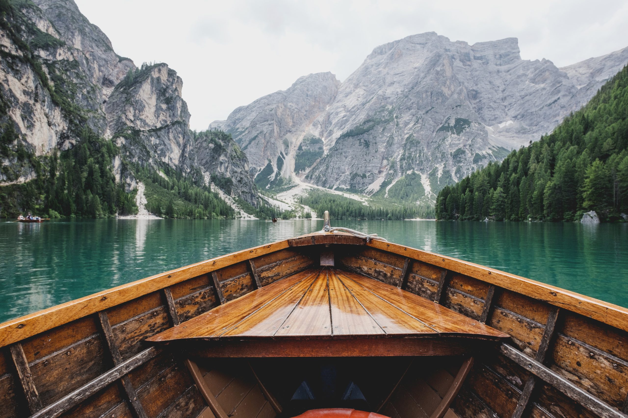 A wooden boat on an emerald lake surrounded by the mountains and forests of the Dolomites